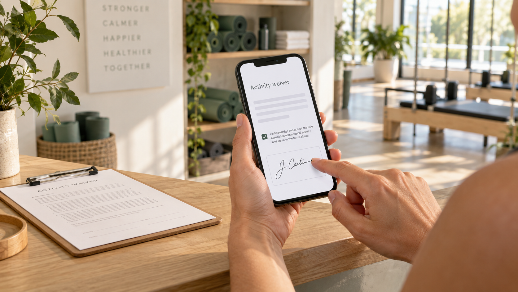 Hands signing a digital activity waiver on a phone beside a paper clipboard in a wellness studio.
